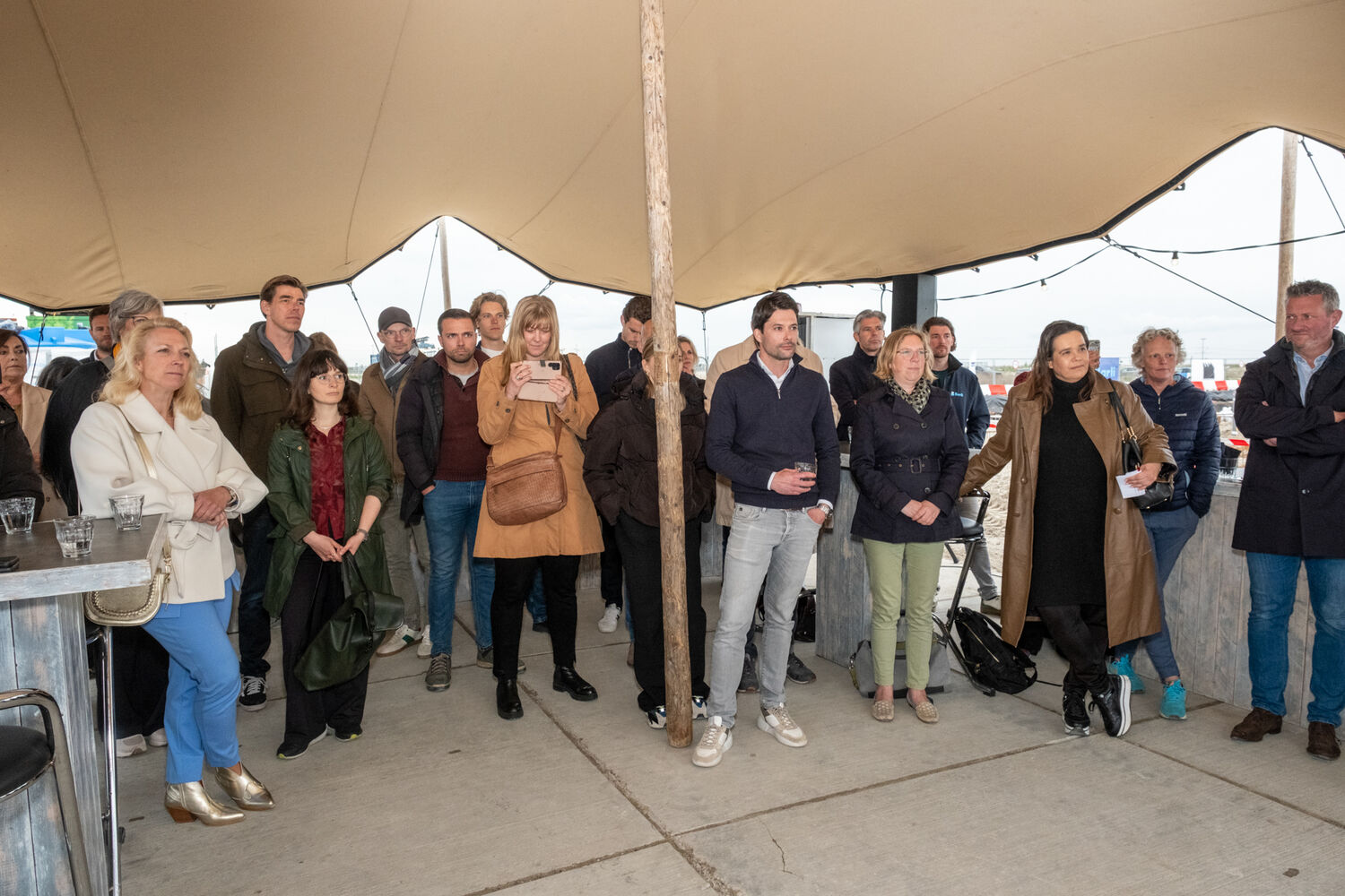 Een groep mensen luistert naar de toespraken tijdens de onthulling van het bouwbord